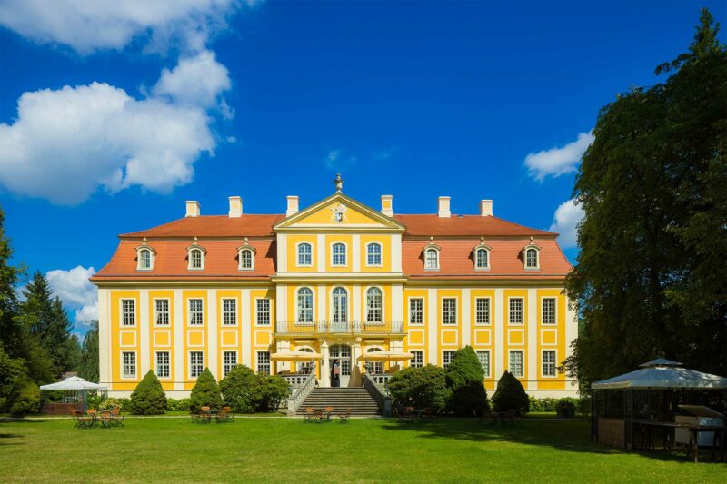 Das Schloss Rammenau bei schönstem Wetter in der Außenansicht, umgeben von grünen Wiesen und Bäumen - Link zur Unterseite Gastspieltätigkeit